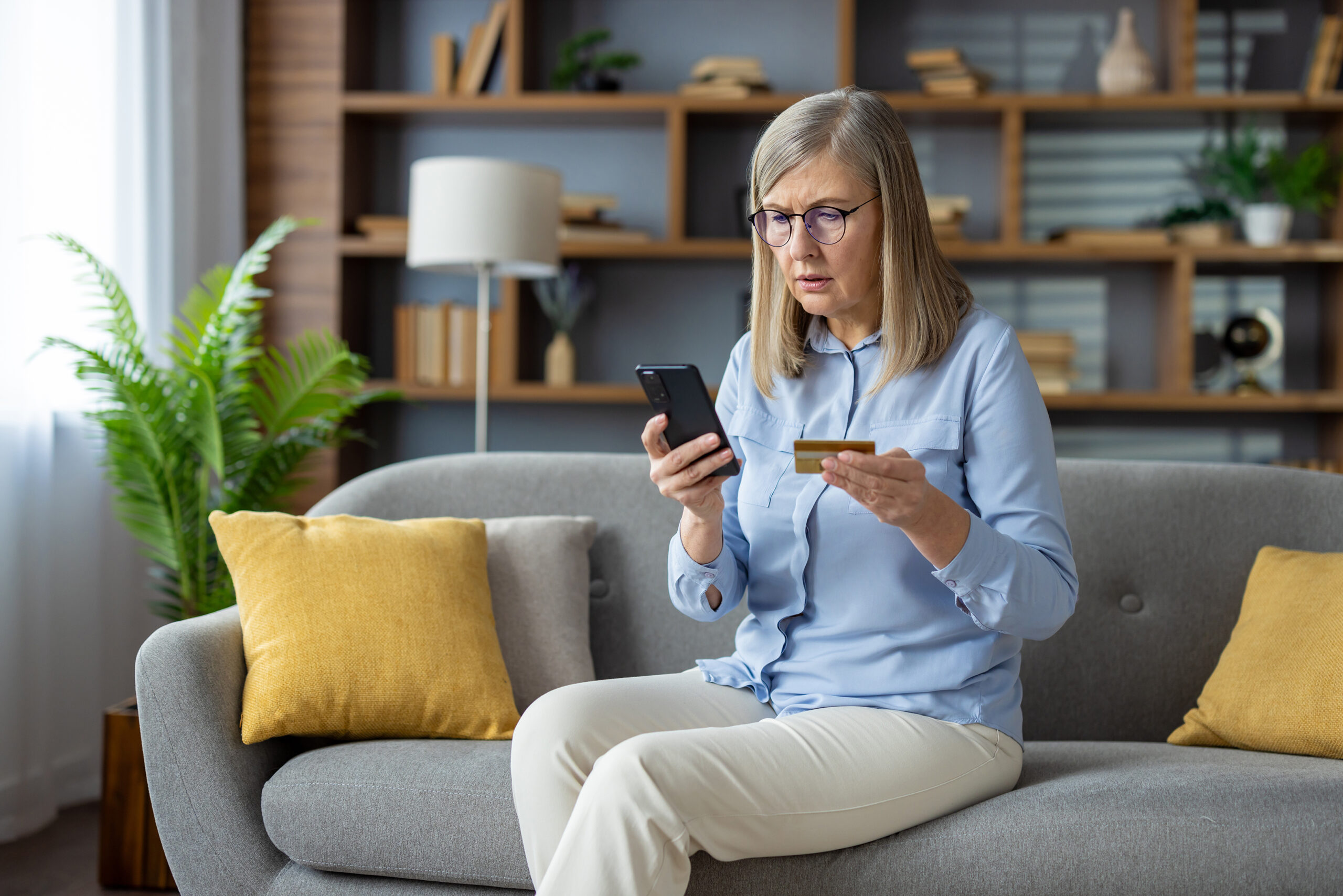 Elder Woman Sitting on Sofa submitting Credit Card information on smartphone.